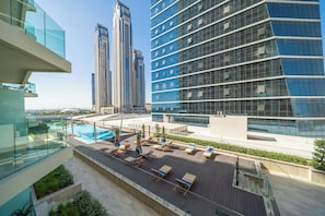 A rooftop pool area with lounge chairs and umbrellas, surrounded by modern buildings with glass facades. - Modern 2BR – Canal-Side Elegance (Dubai)