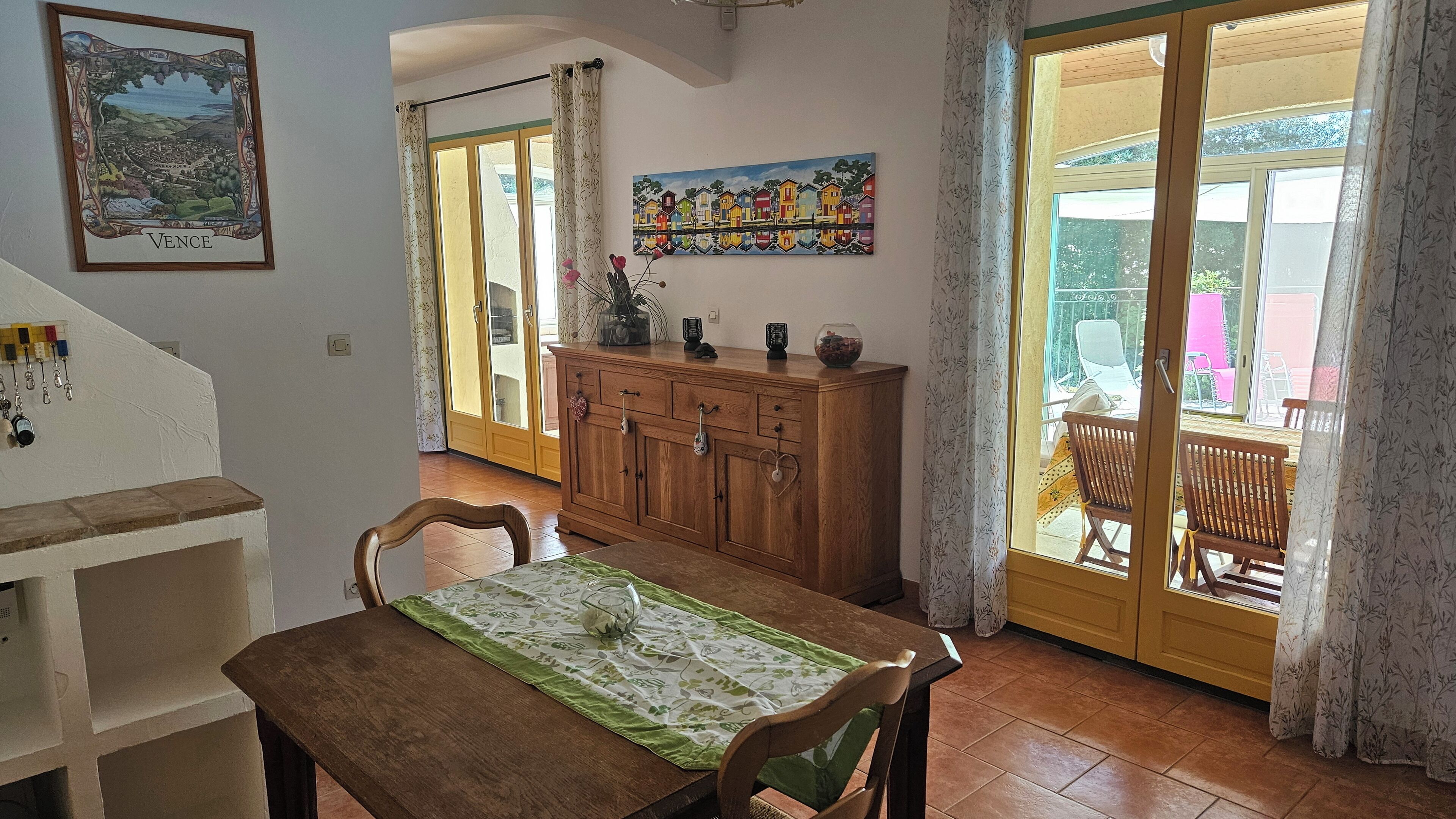 A dining area with a wooden table, chairs, a cabinet, and a painting of houses.