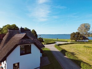 Ein weißes Gebäude mit einem Reetdach, einem gepflasterten Weg und Blick auf ein Gewässer.