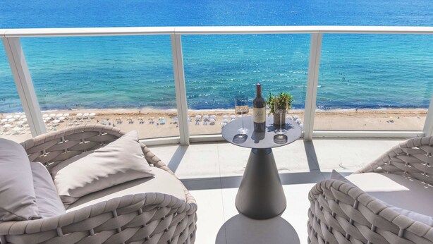 Un balcon agrémenté de meubles en osier, une table avec une bouteille et des verres, et une vue sur la mer et la plage.