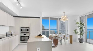 A modern kitchen with a central island, stainless steel appliances, and a dining area with a view of the city. - Oceanfront Hollywood Apartment w/ Balcony & Pool (Hollywood)