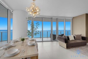 A modern dining area with a view of the sea, a sofa, and a chandelier.