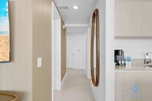 A hotel room with a wooden floor, a kitchen area with a coffee maker, and a view of the beach.