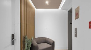 A modern interior with a wooden slat wall, a gray upholstered chair, and a door marked '12R'.