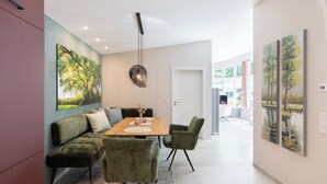 Een moderne eetruimte met een houten tafel, groene fauteuils en kunstwerken aan de muur.
