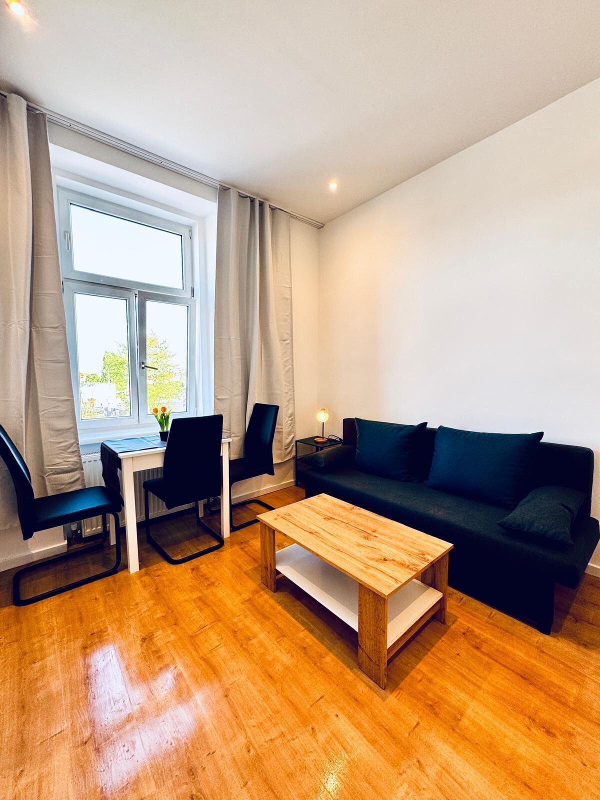 Uma sala de estar moderna com uma mesa de centro de madeira, um sofá verde escuro e duas cadeiras pretas.