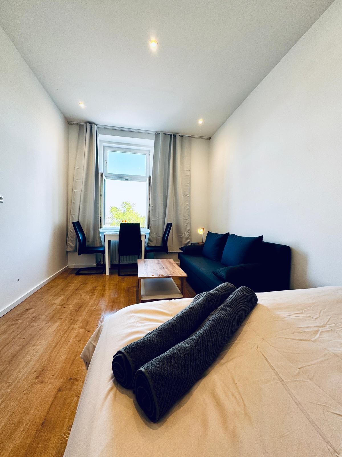 Moderni hotellihuone, jossa on sänky, työpöytä, tuoli ja sohva.