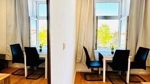 A modern room with a wooden floor, a white table with four black chairs, and a large window with curtains.