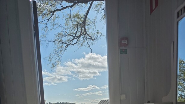 An open door leading to a wooden deck with a view of a lake and picnic tables. - Siaröfortet (Ljustero)