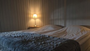 A bedroom with a bed, a nightstand with a lamp, and a wooden floor. - Siaröfortet (Ljustero)