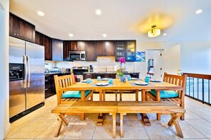 Une cuisine moderne avec des meubles de couleur bois foncé, des appareils électroménagers en acier inoxydable et une table à manger en bois pour quatre personnes.