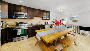 Una cocina moderna con armarios de madera oscura, electrodomésticos de acero inoxidable, una mesa de comedor de madera y un jarrón con flores.