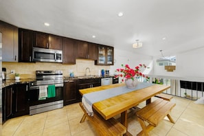 A modern kitchen with dark wood cabinets, stainless steel appliances, a wooden dining table, and a vase with flowers.