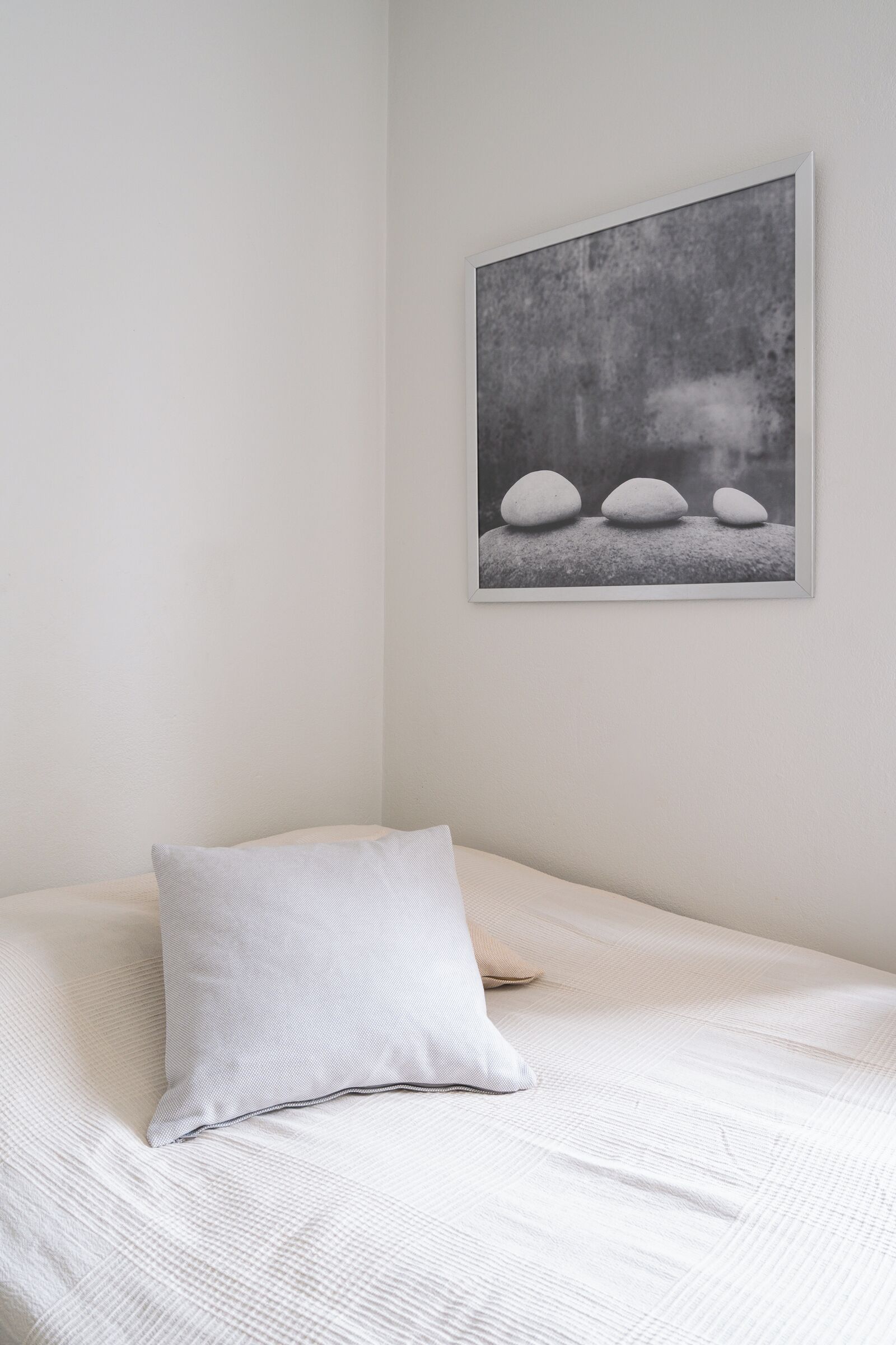 A neatly made bed with a pillow and a framed picture of rocks on the wall.