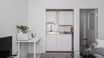 Un espacio habitable compacto con kitchenette, un televisor de pantalla plana, una pequeña mesa con una planta y un sofá gris.