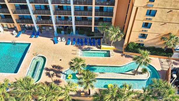 Un hotel con varios balcones, una piscina con sillas de descanso y palmeras.