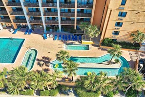 Un hotel con varios balcones, una piscina con sillas de descanso y palmeras.