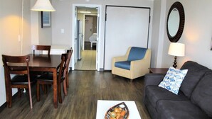 Un salón con un sofá oscuro, una mesa de comedor de madera con sillas, una lámpara y una cesta de pan sobre una mesa.