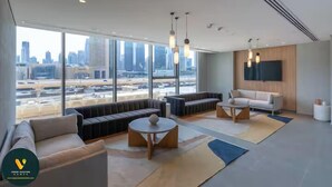 A modern hotel lobby with a large seating area, a television mounted on the wall, and a view of the cityscape through large windows. - Vogue | Downtown with Direct Access to Dubai Mall (Dubai)