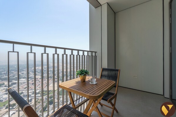 A balcony with a table and chairs, a potted plant, and a view of a cityscape.