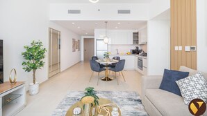 A modern living room with a sofa, coffee table, and a dining area with a table and chairs. - Vogue | Downtown with Direct Access to Dubai Mall (Dubai)