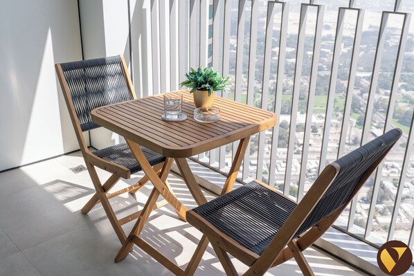 Un balcon avec une table en bois et deux chaises, une plante en pot et un verre d’eau.