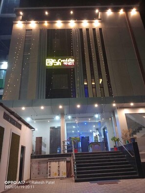 A building with a modern design, featuring a prominent sign with text in a non-Latin script, a staircase leading to the entrance, and a series of lights along the facade. - SHRADDHA SHIVAM RESIDENCY (Chitrakoot)