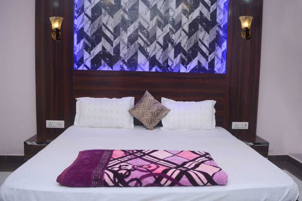 A hotel room with a bed, two wall sconces, a patterned wall, and a woven throw blanket.