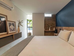 A modern hotel room with a large bed, a built-in TV, a brick accent wall, and a window with a view of greenery.