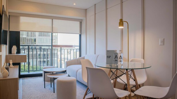 A modern hotel room with a glass table, white chairs, a sofa, a small rug, and a balcony with a city view. - w* | Amazing 2BR w/ Balcony in San Isidro (San Isidro)