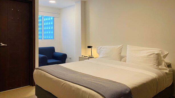 A hotel room with a bed, a chair, a nightstand, and a window with blinds. - w*| Breathtaking 2BR w/ AC in Bocagrande (Cartagena de Indias)