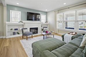 A living room with a fireplace, a television, a sofa, and a window with blinds.