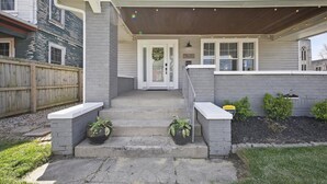 A residential house with a front porch, a wooden deck, and a brick wall.