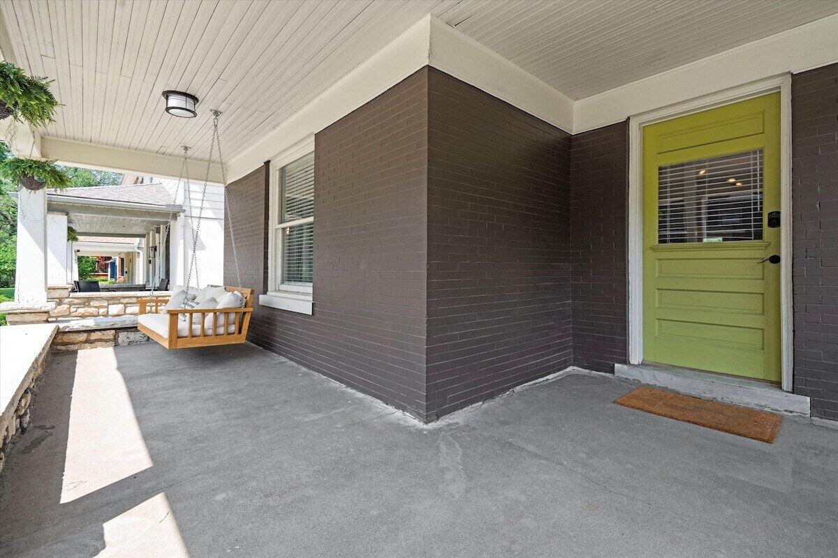 A covered porch with a bench, a green door, and a concrete floor.