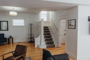 A spacious living room with a staircase, a blue armchair, and a modern pendant light. - Stay on Main - Large Home Near Plaza/Westport (Kansas City)