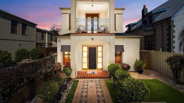 A two-story house with a balcony, a front door, and a small garden with a pathway.