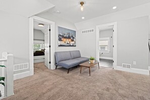 Un salon avec un canapé gris, une table basse en bois et un tableau représentant un paysage urbain accroché au mur.