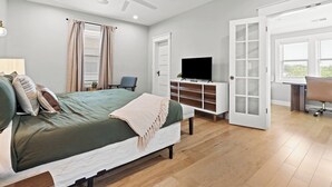 Quarto com cama, televisão, escrivaninha e uma cadeira.