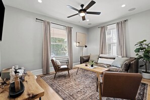 A modern living room with a ceiling fan, a sofa, a coffee table, and a dining table. - Streetcar Central - Hyde Park Home in Midtown KC (Kansas City)