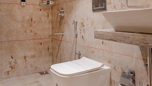 A modern bathroom with a freestanding toilet, a shower area, and a sink with a marble countertop. - Galaxy Royal Suites (Bengaluru)