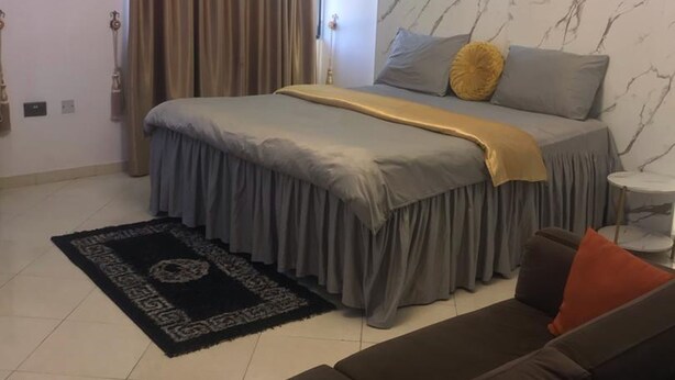 Et moderne soveværelse med en stor seng, en sofa, et lille bord og en væg med marmorlook.