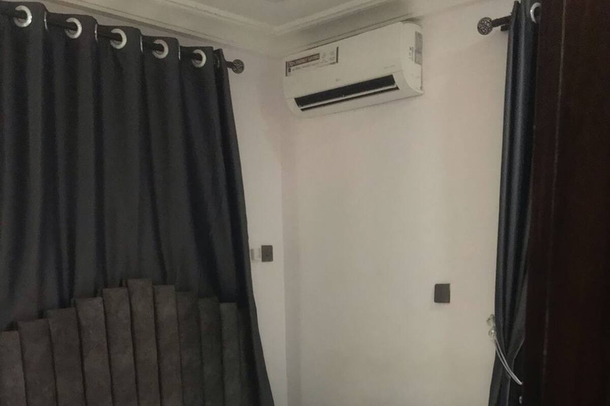 A single bed with a grey headboard, white bedding, and black curtains.