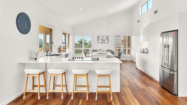 A modern kitchen with a central island, bar stools, a stainless steel refrigerator, and a large clock on the wall.
