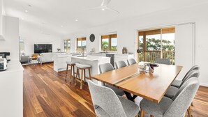 A modern kitchen with a central island, a dining area with a wooden table and grey chairs, and a large window with a view of trees.