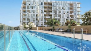 Een zwembad met helderblauw water, omringd door ligbedden en een modern gebouw met meerdere balkons.