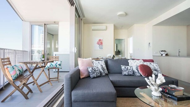 Een moderne woonkamer met een grijze modulaire bank, een glazen salontafel en een balkon met een tafel en stoelen.