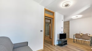 A modern living room with a grey sofa, wooden flooring, a dining area with a table and chairs, and a TV stand. - Residenza I 3 Mori B - Balcony & Mountain Views (Arco)