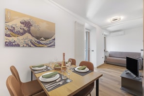 A dining area with a table set for four, a painting on the wall, a sofa, and a TV in the background.