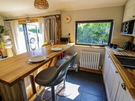 Cocina compacta con encimera de madera, una mesa de comedor con sillas, un reloj y una ventana con vistas al verdor.