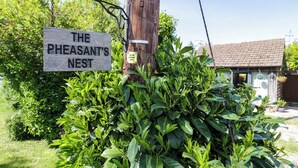 A wooden sign reading "THE PHEASANT'S NEST" attached to a utility pole, surrounded by lush greenery. - The Pheasant's Nest (Malvern)
